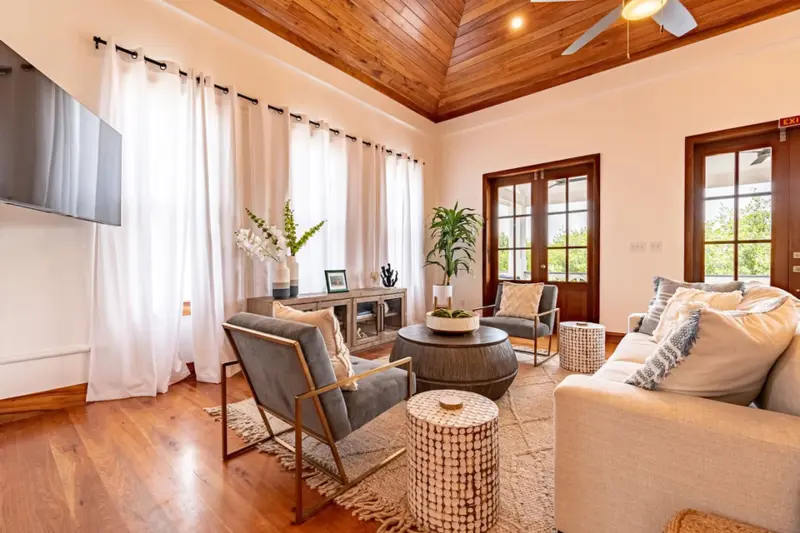 Living room with wood-paneled vaulted ceiling and grey armchairs on a woven rug