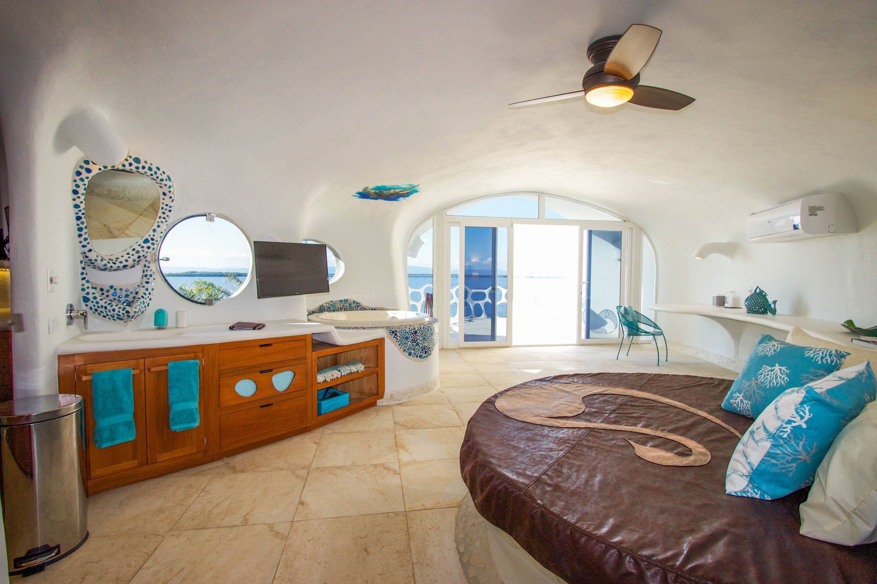 Curved hotel suite with sunken tub, round leather bed and sea view through arched doors