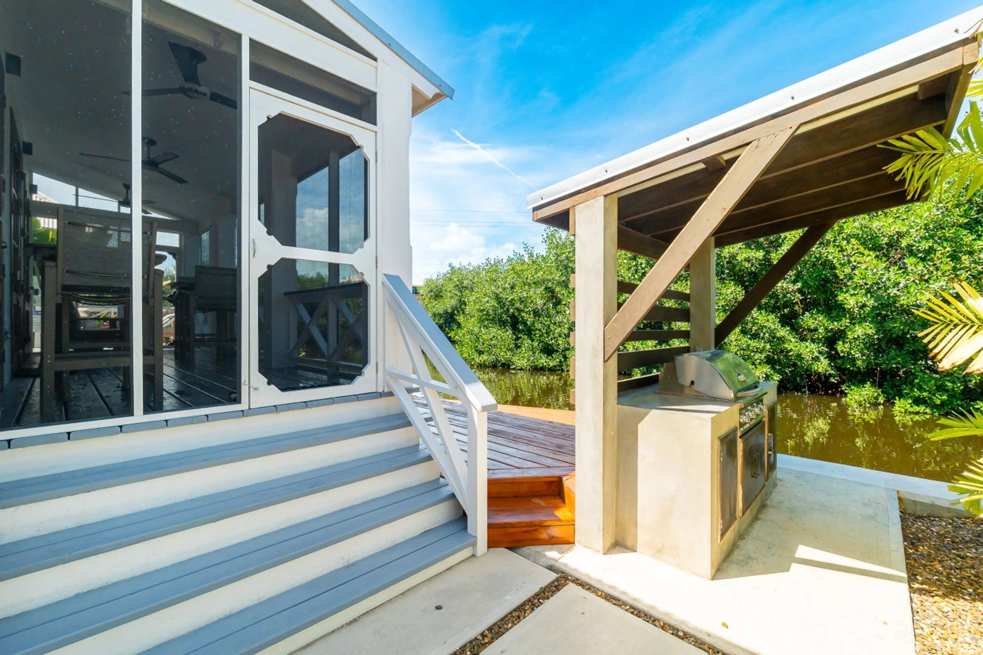 Gray and white staircase beside screened porch, with wood deck and water beyond