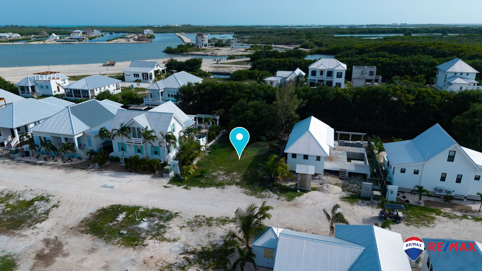 Aerial view of vacant grassy lot between white houses with metal roofs