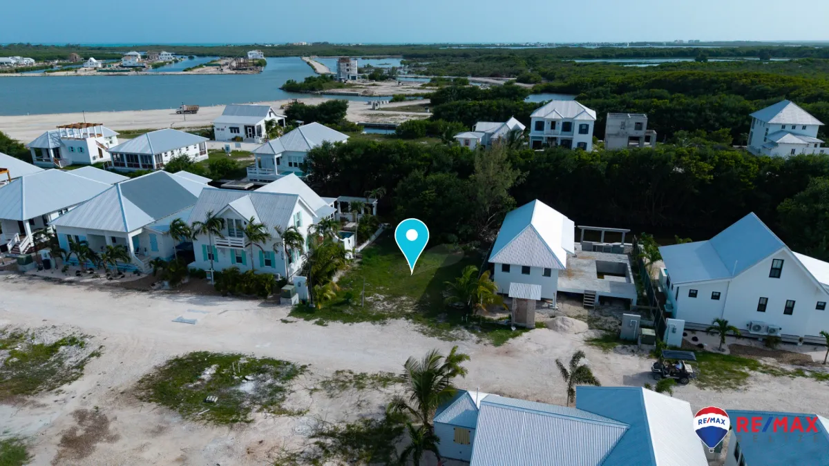 Aerial view of vacant grassy lot between white houses with metal roofs