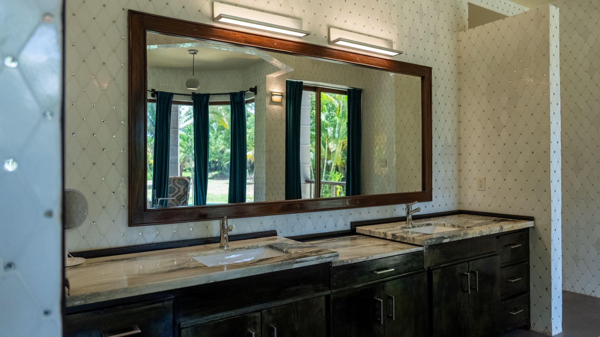 Bathroom double vanity with marble counters, dark cabinets and large wall mirror
