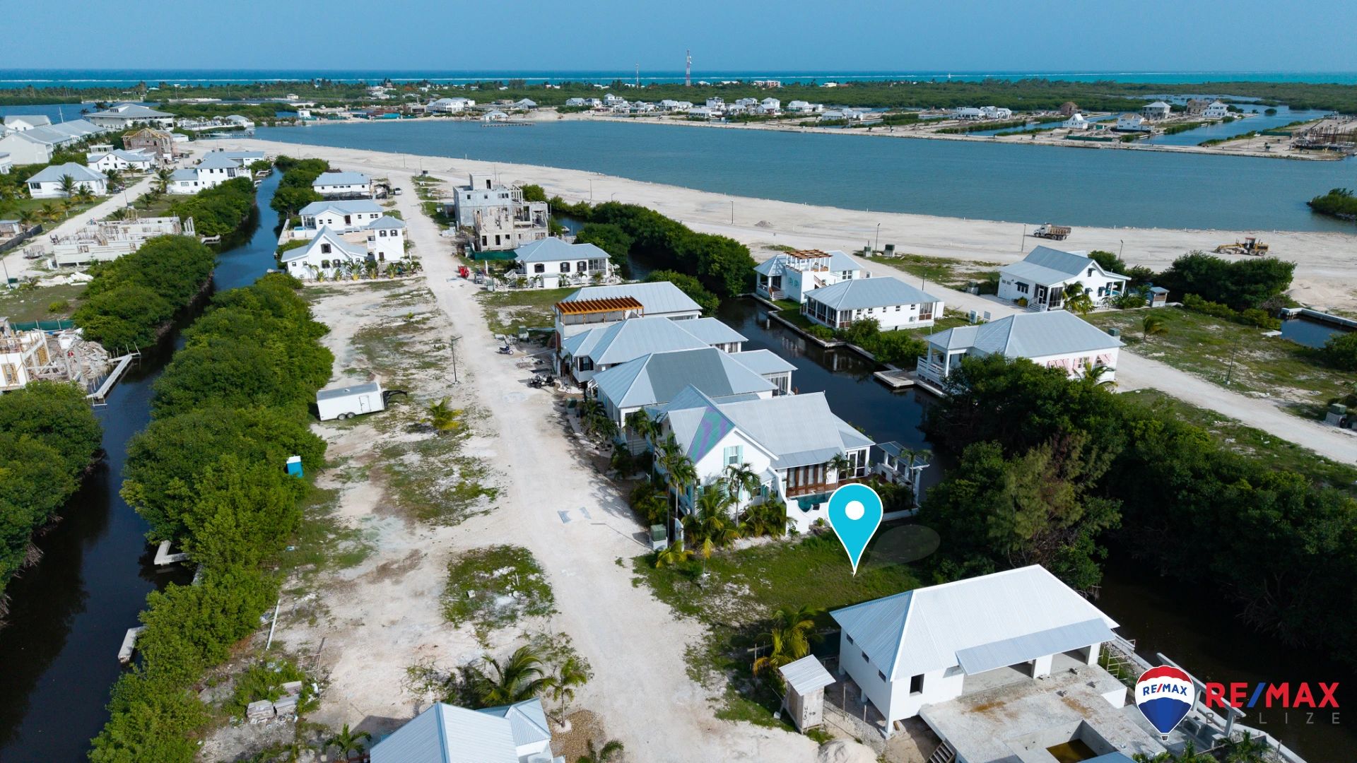 Aerial view of coastal homes along a canal with a marker on a grassy lot