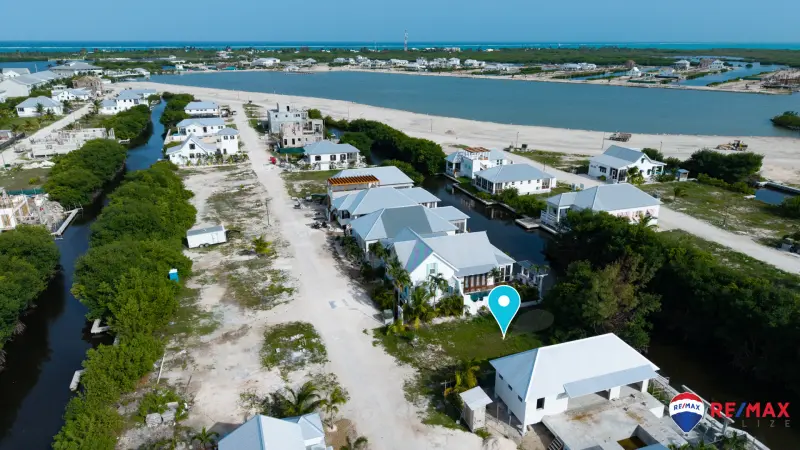 Aerial view of coastal homes along a canal with a marker on a grassy lot