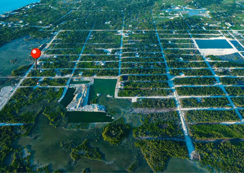 Aerial view of gridded lots with scattered houses beside green water and mangroves