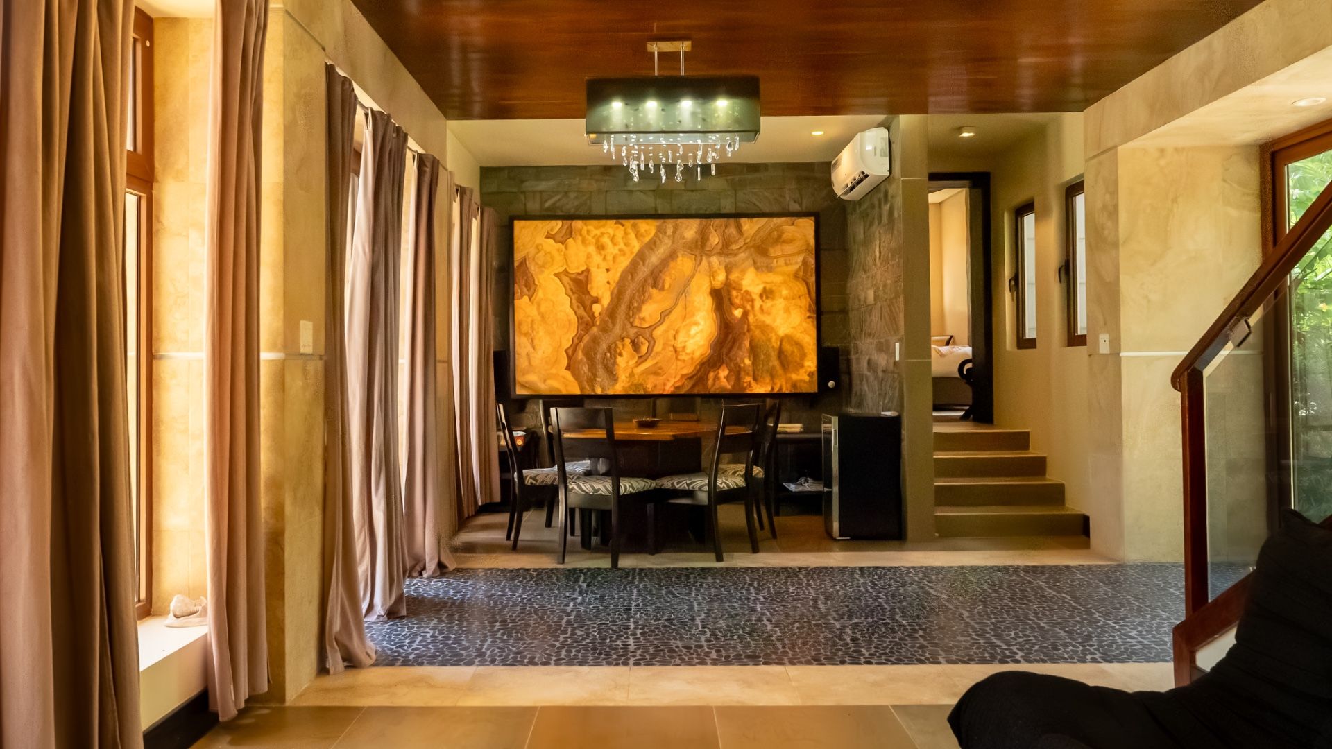 Dining area with round wooden table, patterned chairs and backlit onyx wall panel