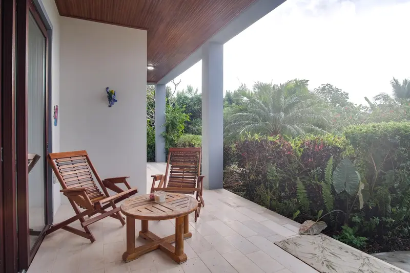 Covered terrace with wooden lounge chair and round side table among tropical greenery