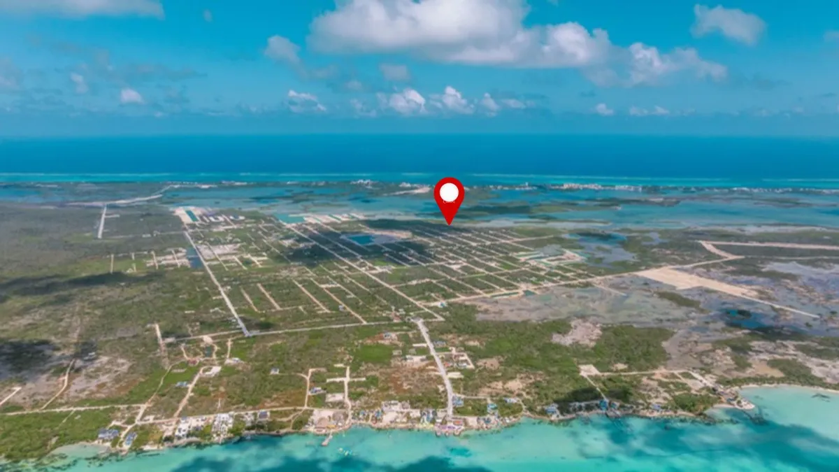 Aerial view of subdivided lots with red location pin above turquoise sea