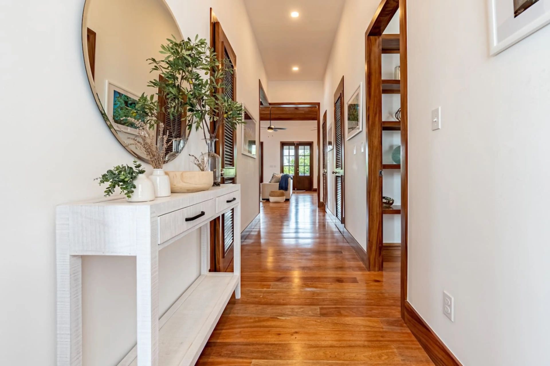 Long hallway with polished wood floors, white console table and potted olive branches