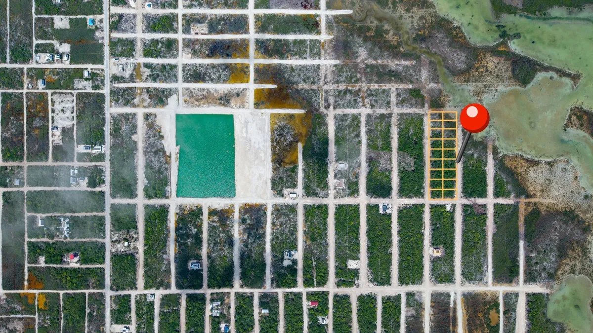 Aerial view of subdivided lots with dirt roads, scrub vegetation and a turquoise pond